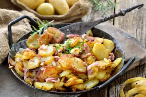 Patatas con bacon y queso, doradas y crujientes, servidas en una sartén de hierro fundido. Un plato perfecto para compartir.