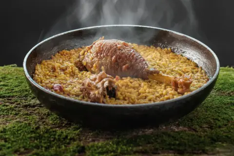 Arroz meloso con pitu de caleya, humeante y servido en paellera sobre un lecho de musgo.