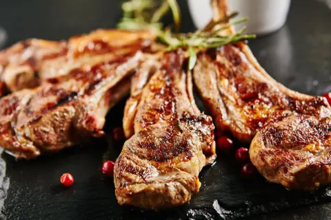 Chuletillas al sarmiento, jugosas y doradas, servidas con bayas rojas y romero sobre pizarra.