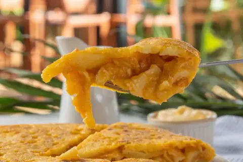 Un tenedor levanta un trozo jugoso de pincho de tortilla, mostrando su interior de patatas y huevo.