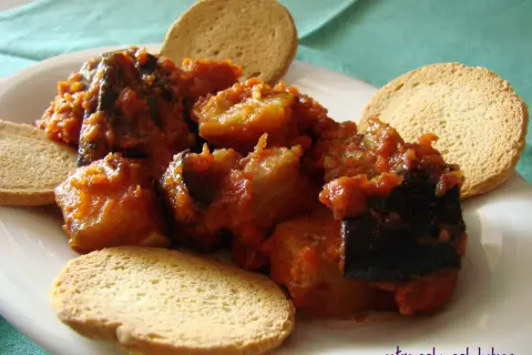 Berenjenas con tomate, un plato casero servido con tostas crujientes.