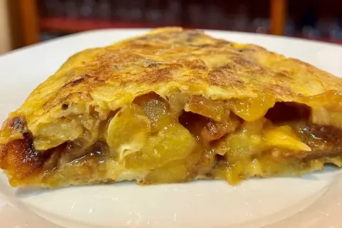 Un trozo jugoso de tortilla de patatas, con patatas tiernas y huevo dorado, servido en un plato blanco.