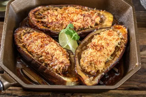 Berenjenas rellenas airfryer doradas y gratinadas, servidas en una sartén de hierro fundido con una rodaja de lima.