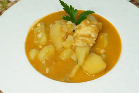 Un plato de patatas con bacalao en una salsa naranja, decorado con perejil.