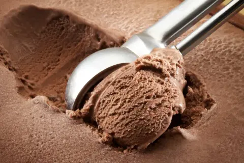 Cuchara saca una porción generosa de helado de chocolate casero, con textura cremosa y color intenso.