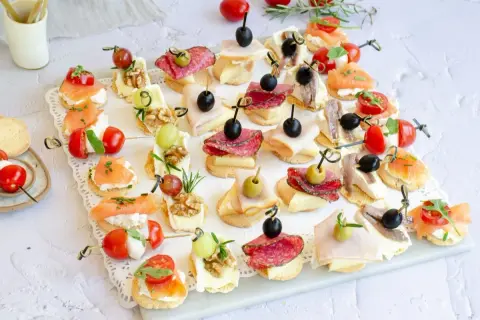 Variedad de canapés fríos fáciles y baratos: salmón, salami, jamón, queso, aceitunas, tomates cherry y más, perfectos para cualquier ocasión.