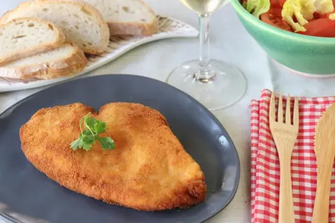 Un delicioso escalope de pollo dorado, servido con pan, ensalada y vino blanco.