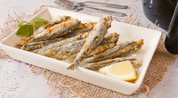 Boquerones en freidora de aire, dorados y crujientes, servidos en plato blanco con limón y perejil.