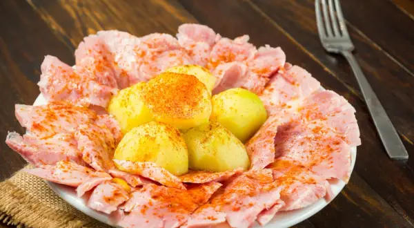 Plato de lacon con cachelos, patatas cocidas y pimentón, servido sobre una mesa de madera.
