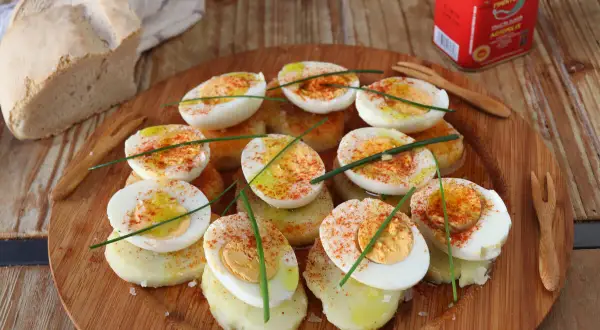 Deliciosos huevos a la gallega, cortados por la mitad y espolvoreados con pimentón, sobre rodajas de patata.