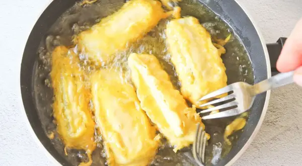 Soldaditos de pavia dorándose en aceite caliente. Un tenedor los voltea para una fritura perfecta.