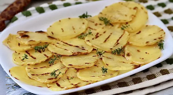 Deliciosas patatas a la plancha, finamente cortadas y con marcas de parrilla, adornadas con ramitas de tomillo fresco.