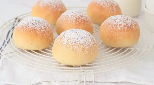 Seis deliciosas cocas de patata espolvoreadas con azúcar glas sobre una rejilla.
