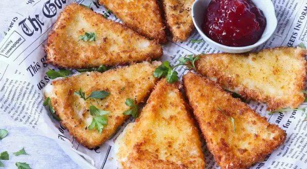 Triángulos de queso frito crujientes, servidos con un tazón de mermelada de frutos rojos.