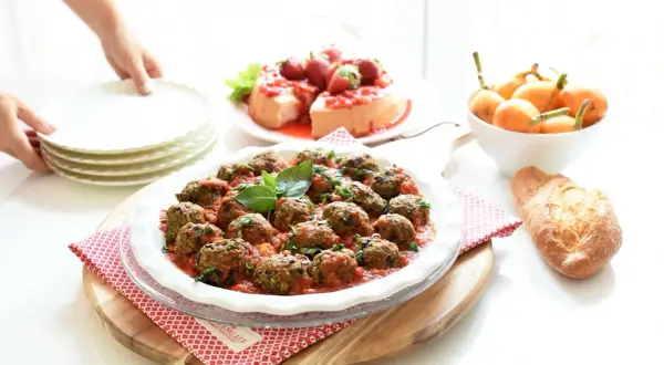 Albondigas de berenjenas en salsa roja, decoradas con albahaca, junto a un postre de fresas y pan.