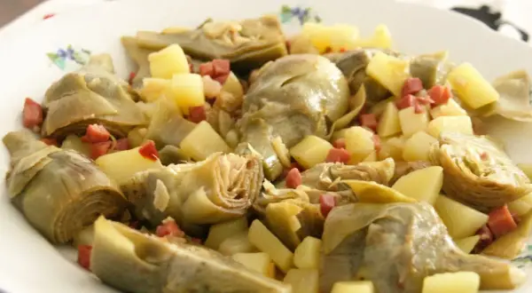 Plato de alcachofas tiernas y trocitos de patata, salpicado con dados de jamón serrano. Un bocado delicioso.