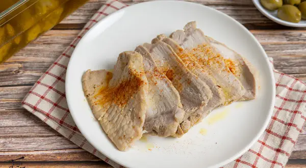 Lomo de orza tierno y jugoso, cortado en lonchas y espolvoreado con pimentón. Servido en plato blanco sobre mantel a cuadros.