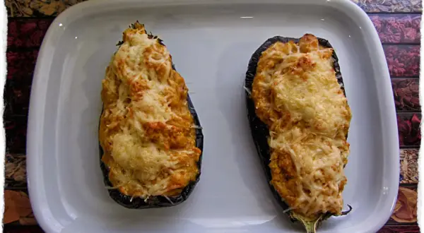 Dos berenjenas rellenas de gambas, gratinadas con queso, listas para disfrutar.