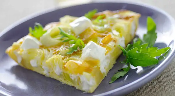Porción de tortilla con puerros y queso de cabra, decorada con rúcula. Ideal para tus recetas con puerros.