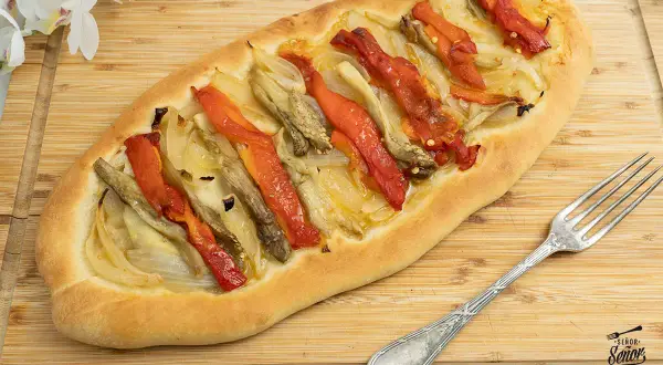 Coca de recapte con verduras asadas, pimientos rojos y cebolla sobre una base de pan rústico.