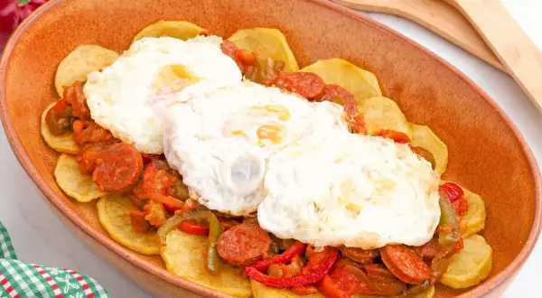 Huevos a la riojana servidos en una cazuela de barro, con patatas, chorizo y pimientos.
