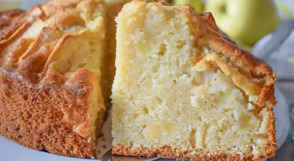 Un trozo de bizcocho de manzana casero, con trozos de fruta visibles en su interior tierno y dorado.