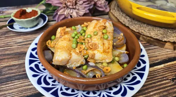 Bacalao a la gallega con patatas, guisantes y ajo frito en cazuela de barro. Un plato tradicional lleno de sabor.