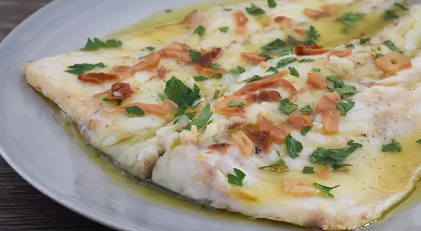 Lubina a la donostiarra, un plato de pescado blanco tierno bañado en aceite de oliva con láminas de ajo dorado y perejil fresco.