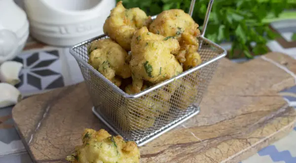 Buñuelos de bacalao dorados y crujientes, servidos en una cesta metálica. Perfectos para picar.