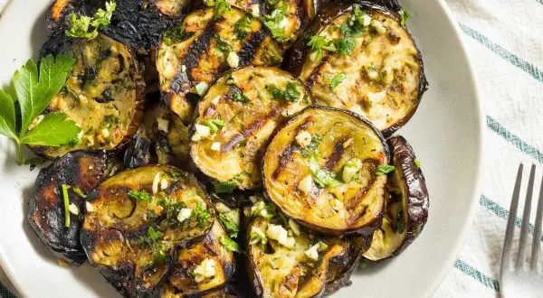 Rodajas de berenjena a la plancha, doradas y tiernas, con ajo picado y perejil fresco. Un plato delicioso y saludable.