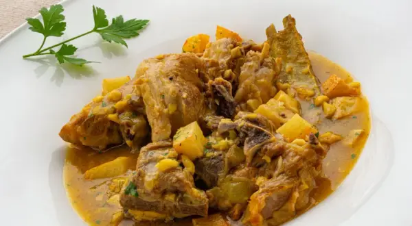 Choto al ajillo, un guiso tierno de cabrito con patatas y un toque de ajo, servido en un plato blanco.