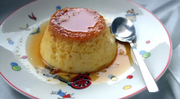 Delicioso flan de huevo casero, la receta de la abuela que nunca falla. Servido en un plato con dibujos infantiles y una cuchara lista para disfrutar.