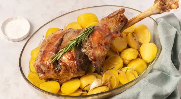Pierna de cordero al horno con patatas doradas, ajo y romero. Un plato principal jugoso y aromático.
