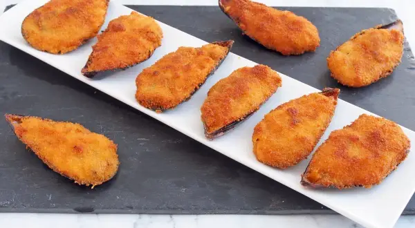 Mejillones tigre receta: mejillones rebozados y fritos, dorados y crujientes, servidos en una bandeja blanca sobre una pizarra.