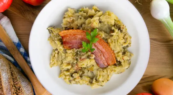 Un plato de trinxat de montaña con crujiente panceta y perejil. Acompañado de pan rústico, tomates y cebolletas.
