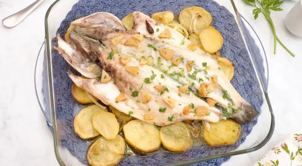 Lubina al horno con patatas y ajo, recién salida del horno, lista para servir.