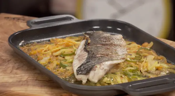 Filete de corvina a la roteña, con verduras salteadas en una sartén de hierro fundido.