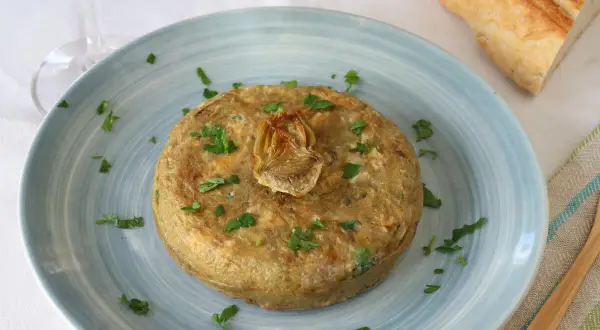 Tortilla de patatas con alcachofas de bote, decorada con perejil. Ideal para tus recetas con alcachofas de bote.