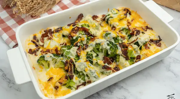 Delicioso brocoli al horno gratinado con queso y tocino crujiente, servido en una fuente blanca.