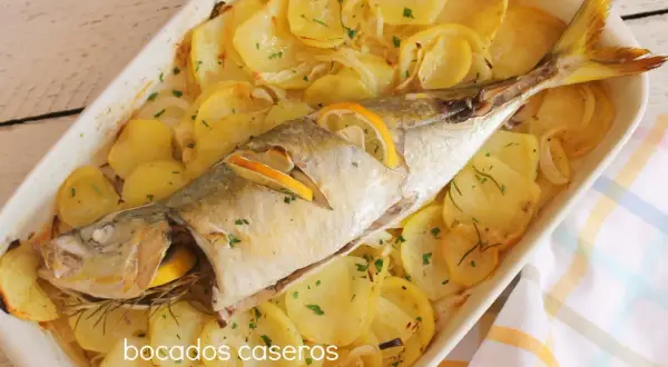 Un delicioso chicharro al horno con patatas, limón y romero, listo para servir.