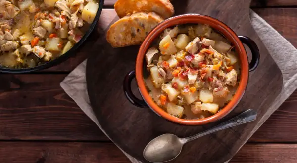 Un reconfortante guiso de pollo con patatas de la abuela, servido en cazuela de barro con pan tostado.
