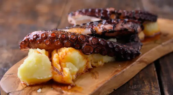 Pulpo tierno con patatas y pimentón, servido en tabla de madera.