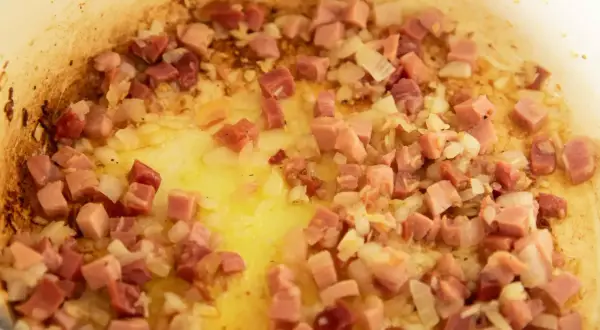 Guisantes con jamón, la receta de la abuela en plena cocción. Cebolla y taquitos de jamón dorándose en la sartén.