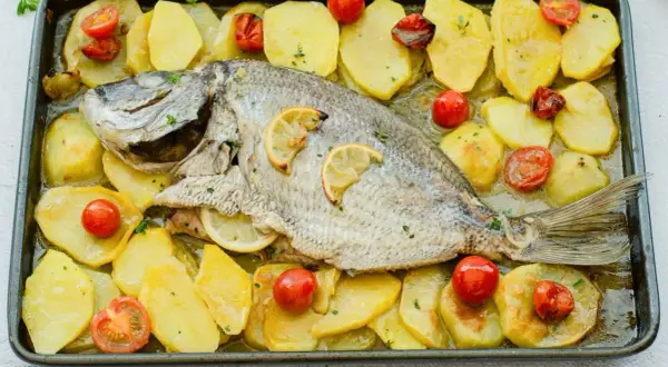 Delicioso sargo al horno con patatas y tomates cherry, listo para servir.