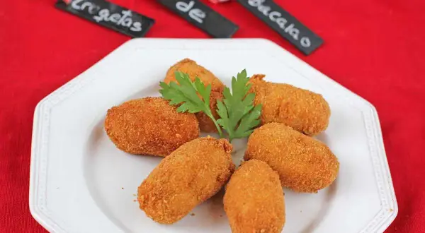 Croquetas de bacalao doradas y crujientes, servidas en un plato blanco con perejil.