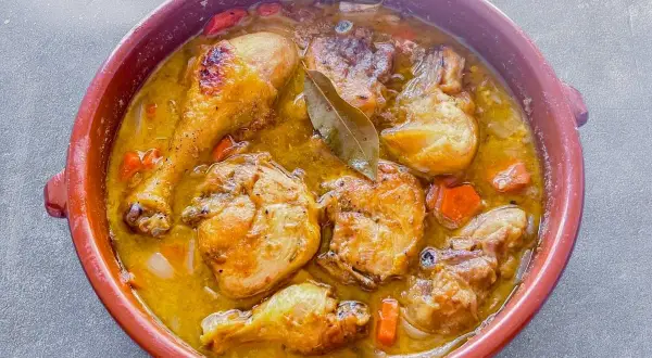 Delicioso pollo de corral guisado en cazuela de barro con zanahorias y laurel.