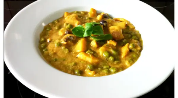 Plato de jibia en salsa de almendras, con guisantes y trozos de patata, decorado con una hoja verde.