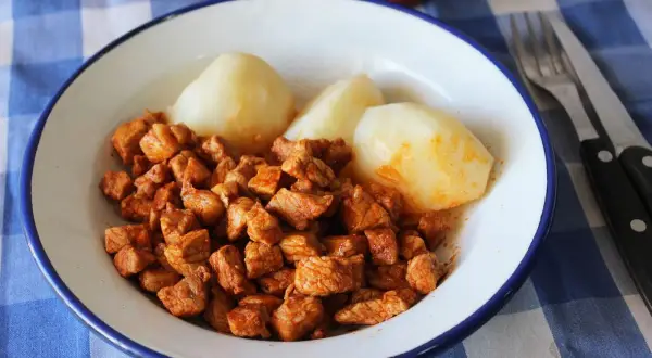 Plato de zorza con patatas cocidas, servido en un cuenco blanco con borde azul sobre un mantel de cuadros.