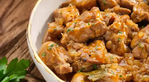 Un delicioso plato de caldereta de cordero, con trozos tiernos de carne en una salsa dorada y aromática, adornado con perejil fresco.