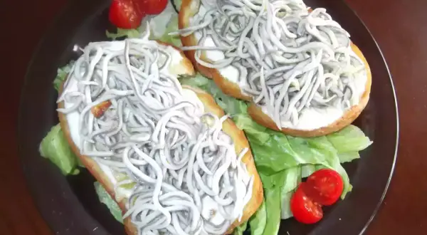 Dos tostas de gulas sobre lechuga y tomate cherry, un bocado delicioso.